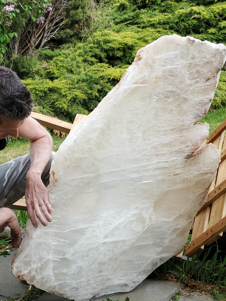 Aaron K Metz standing beside a large hand-carved and polished selenite crystal sculpture from Jalisco, Mexico