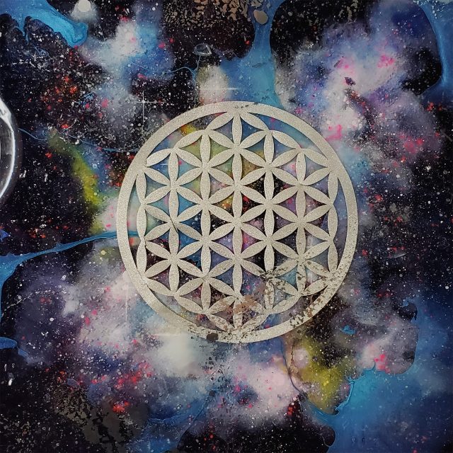 Luminous cosmic artwork 'Sacred Cosmos 13' featuring silver Flower of Life symbol suspended in a blue-green nebula with photoluminescent pigments and crystal infusions by artist Aaron K Metz