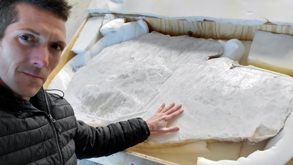 Artist standing beside a 150-pound cleaned selenite crystal slab packaged in an open shipping crate