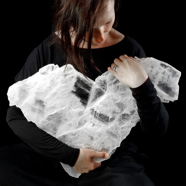 Woman holding a large, translucent heart-shaped selenite ice crystal against a black background