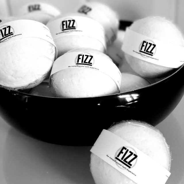 Collection of white FIZZ bath bombs with selenite crystals inside displayed in a black bowl